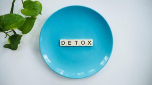 Minimalist concept of detox with letter tiles on a turquoise plate and green leaves.